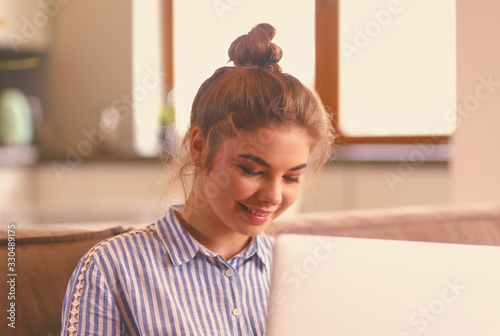 Happy brunette woman sitting on sofa with laptop photo