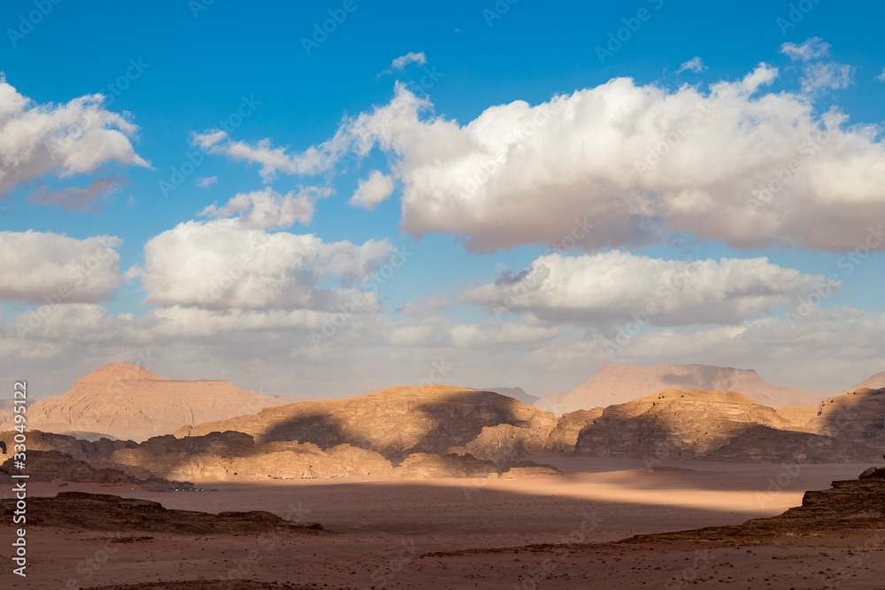 Kingdom of Jordan, Wadi Rum desert, sunny winter day scenery landscape with white puffy clouds and warm colors. Lovely travel photography. Beautiful desert could be explored on safari. Colorful image Kingdom of Jordan, Wadi Rum desert, sunny winter day scenery landscape with white puffy clouds and warm colors. Lovely travel photography. Beautiful desert could be explored on safari. Colorful image