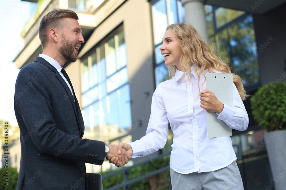 Image of collegues discussing documents and shaking hands near office.