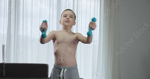 Happy child doing sports at home, boy fitness training dumbbells