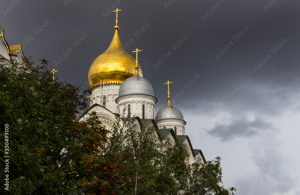 Golden domes of the Arkhangelsk Cathedral of the Moscow Kremlin against a dark stormy sky.