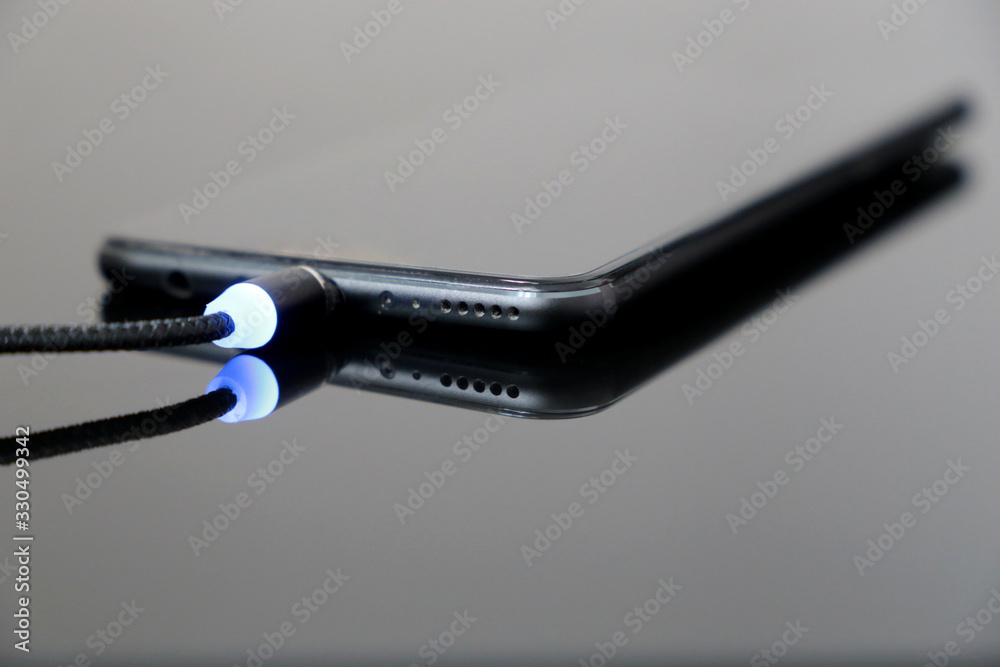 Black smartphone is charging on a dark glass surface. Mobile phone with with magnetic type C cable Black smartphone is charging on a dark glass surface. Mobile phone with with magnetic type C cable