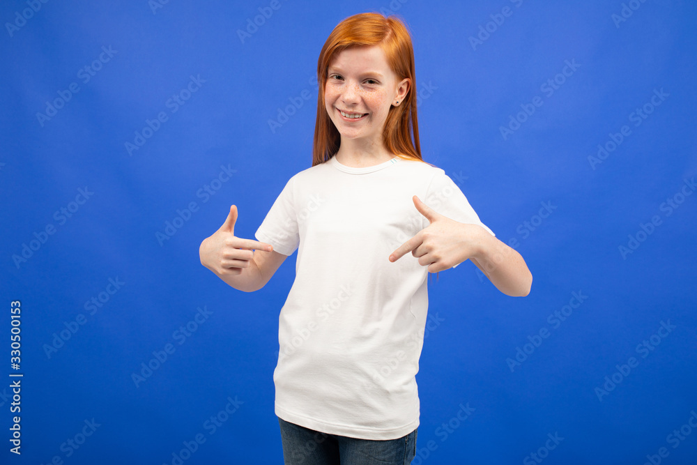charming red-haired teenager girl in a white T-shirt with a mockup on a blue studio background charming red-haired teenager girl in a white T-shirt with a mockup on a blue studio background