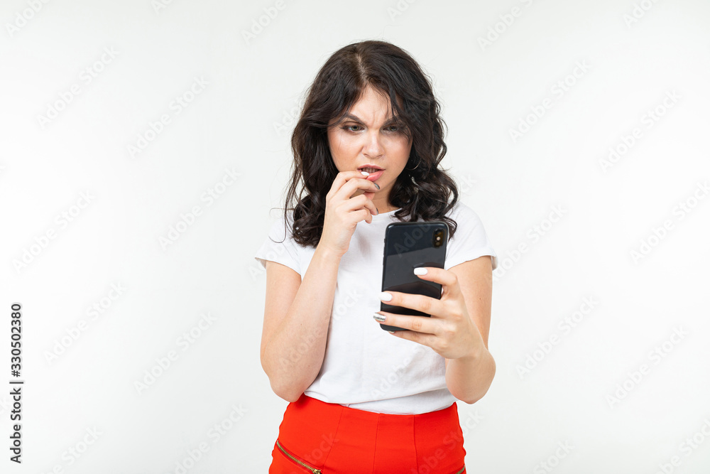 girl in a white T-shirt thoughtfully reads a message on her smartphone on a white studio background with copy space girl in a white T-shirt thoughtfully reads a message on her smartphone on a white studio background with copy space
