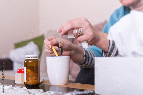 A very sick woman with temperature drinks warm tea