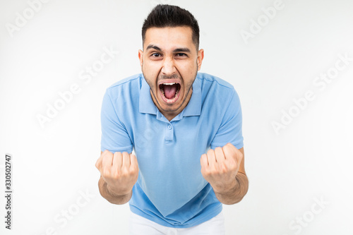 handsome caucasian man in a blue t-shirt holds fists for good luck on a white studio background