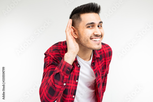 brunette guy in a checkered shirt wide open eavesdrops on a conversation on a white studio background