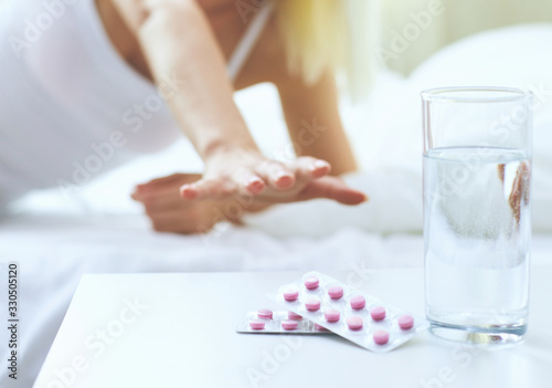Young beautiful woman with pills sitting on bed in bedroom