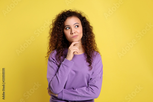 Pensive African-American woman on yellow background. Thinking about difficult question photo