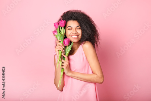 Young african woman with flowers on pink background. Women's day concept #330506122