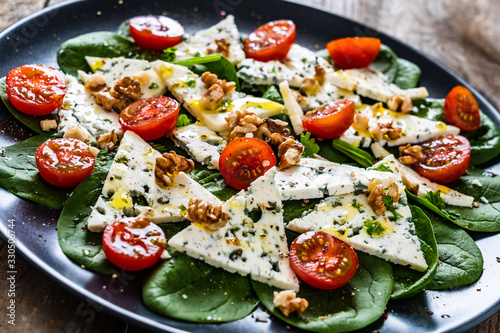 Fresh salad - blue cheese, cherry tomatoes, spinach, walnuts on wooden background