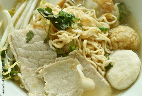 boiled yellow instant noodles topping slice pork and ball in clear soup on bowl