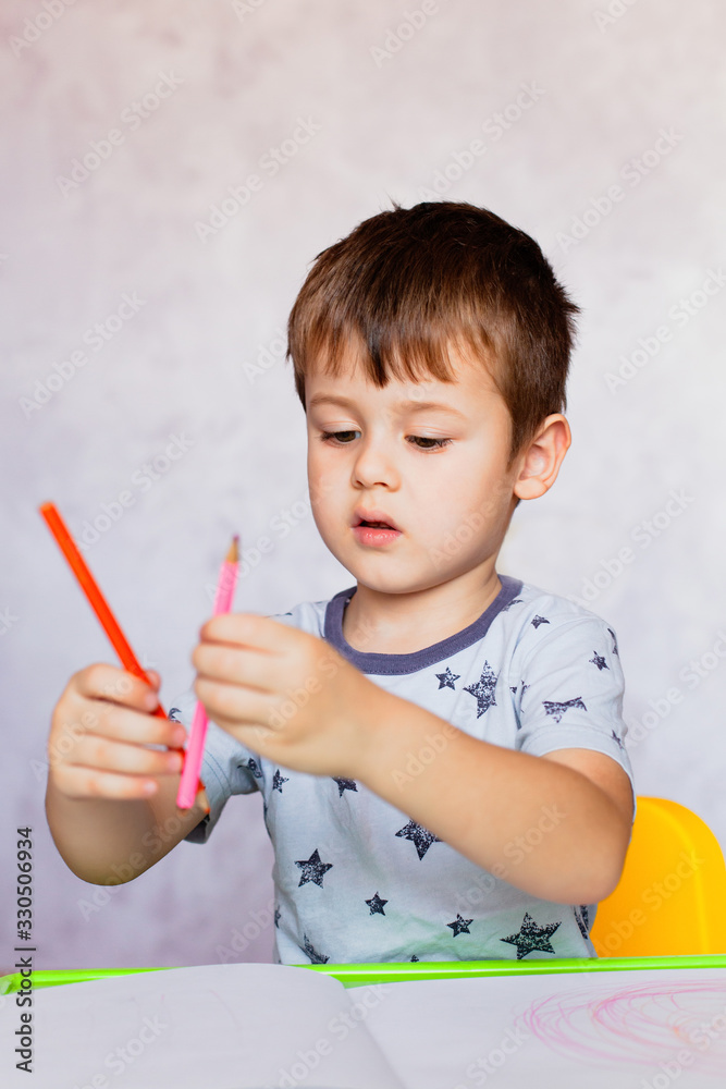 Little boy is holding color pencils. Boy, drawing a picture for fathers day. Small boy draws at the table. Little boy is holding color pencils. Boy, drawing a picture for fathers day. Small boy draws at the table.