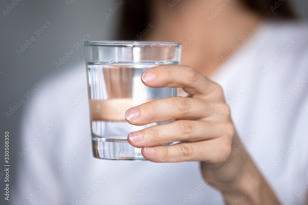 Close up focus on glass of pure distilled water in female hands. Young thirsty woman holding clear liquid aqua, ready drink, prevent organism from dehydration, body balance, healthcare, refreshment. Close up focus on glass of pure distilled water in female hands. Young thirsty woman holding clear liquid aqua, ready drink, prevent organism from dehydration, body balance, healthcare, refreshment.