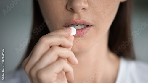 Close up cropped image unhealthy young woman taking round pill  suffering from ache  painful feelings. Unhappy brunette lady taking painkiller  antibiotic or antidepressant  having depression.