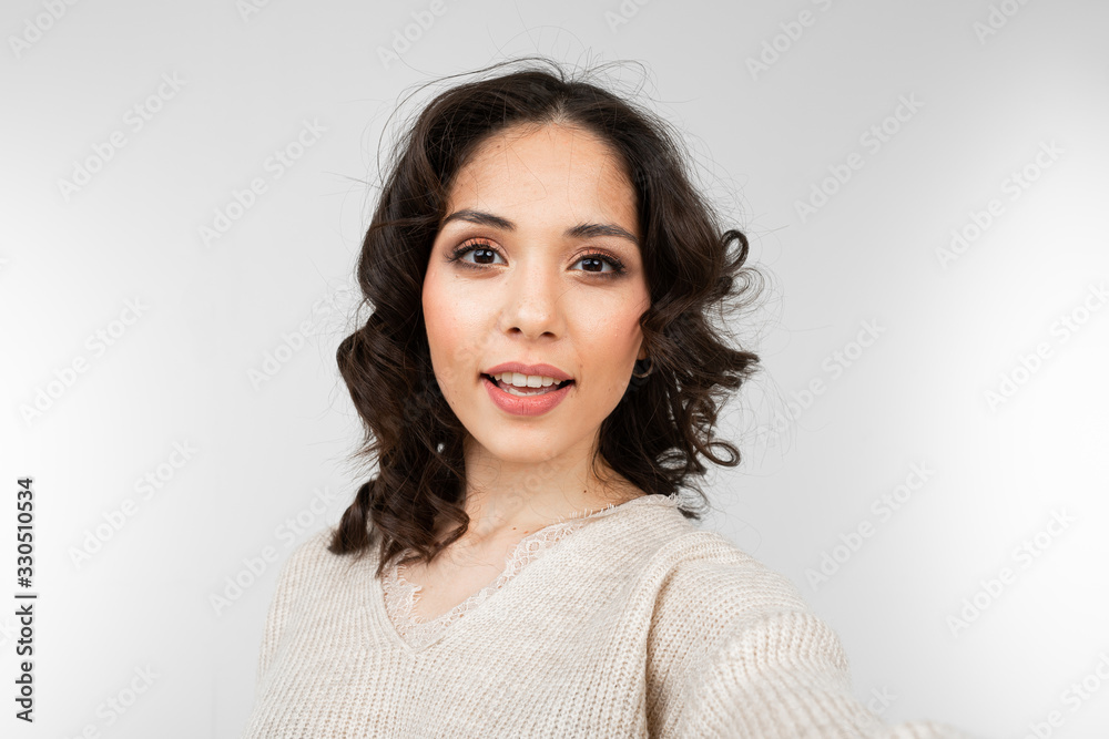 Beautiful brunette girl with makeup makes selfie on a gray studio background Beautiful brunette girl with makeup makes selfie on a gray studio background