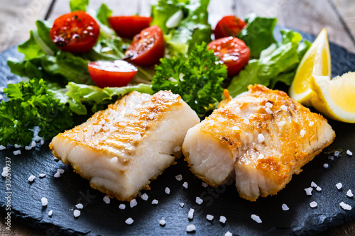 Fish dish - fried cod fillet with vegetables on wooden table