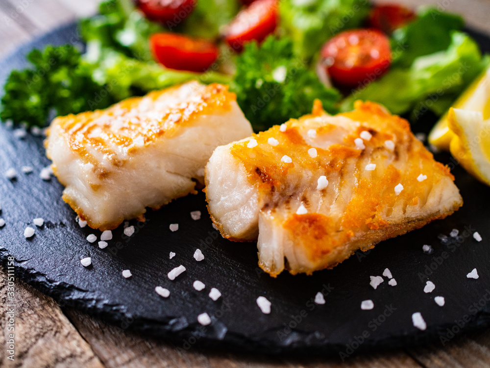 Fish dish - fried cod fillet with vegetables on wooden table Fish dish - fried cod fillet with vegetables on wooden table