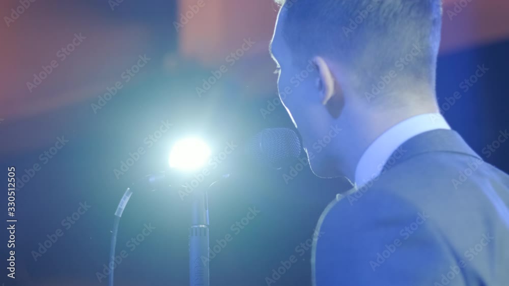 Man singing song in microphone during performance on stage on rock concert. Close up man rock star singer on music concert on colorful light background Man singing song in microphone during performance on stage on rock concert. Close up man rock star singer on music concert on colorful light background
