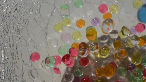 Multicolored hydrogel balls fill a glass vase, close-up. Movement: fall, bounce