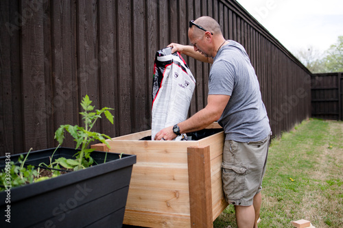 Man pours topsoil into a wooden backyard container garden