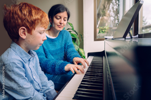 Piano teacher woman teaching a little boy at home piano lessons. Family lifestyle spending time together indoors. Children with musical virtue and artistic curiosity. Educational musical activities.
