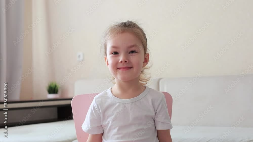 Four years little girl with pretty face smiling looking at camera at home sitting on chair near sofa, waving her head. Four years little girl with pretty face smiling looking at camera at home sitting on chair near sofa, waving her head.