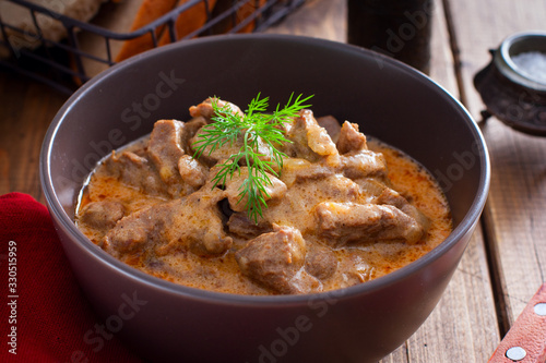 Traditional beef stroganoff in a ceramic bowl on a wooden table, selective focus