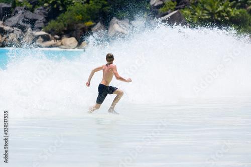 Young teenager boy enjoys summer holiday in sea. The kid runs away from huge wave.