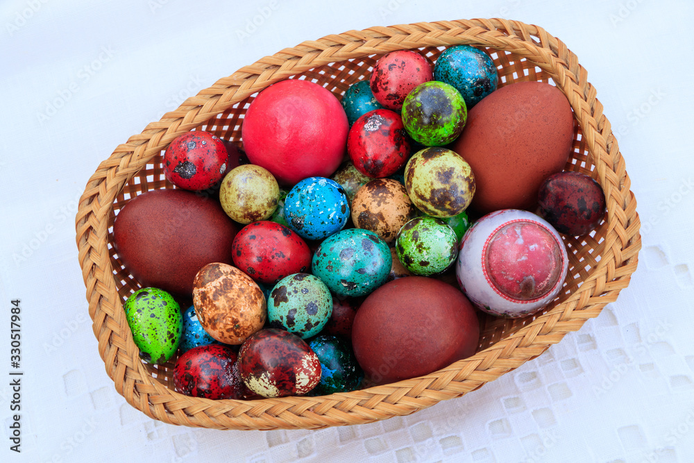 Basket of straws with Easter eggs painted in different colors and different sizes on a tablecloth Basket of straws with Easter eggs painted in different colors and different sizes on a tablecloth