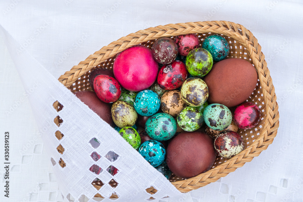 Basket of straws with Easter eggs painted in different colors and different sizes on a tablecloth Basket of straws with Easter eggs painted in different colors and different sizes on a tablecloth