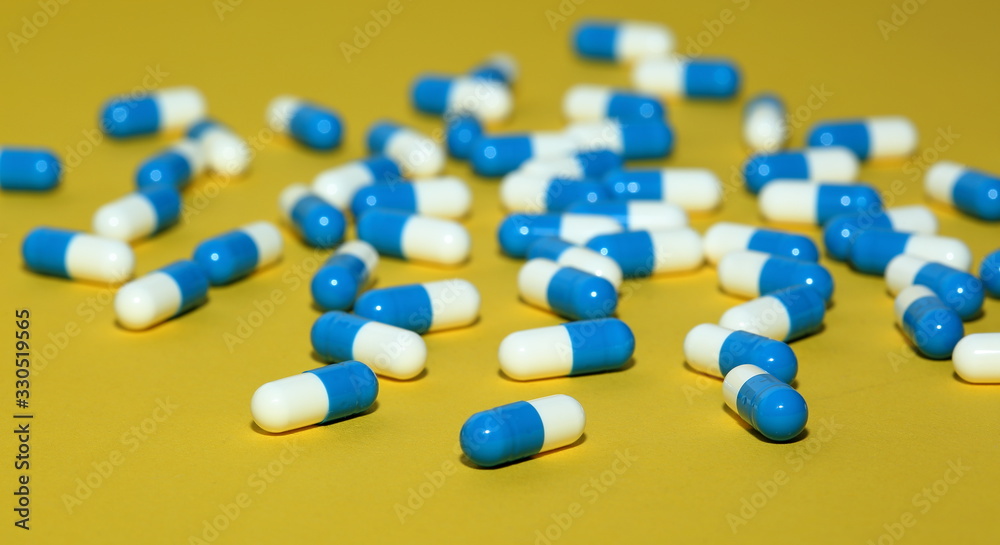 ouble colored white and blue capsules tablets pills on yellow background macro ouble colored white and blue capsules tablets pills on yellow background macro