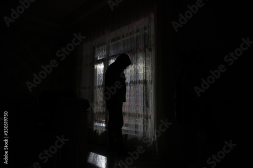 Silhouette of a man standing at a window inside the room. Fantasy picture with old vintage lantern at the window inside dark room.