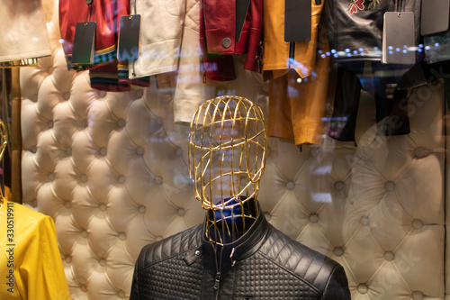 The front of a clothing store. Metalic lifeless mannequins stand in the background in the store with various items. Close up.