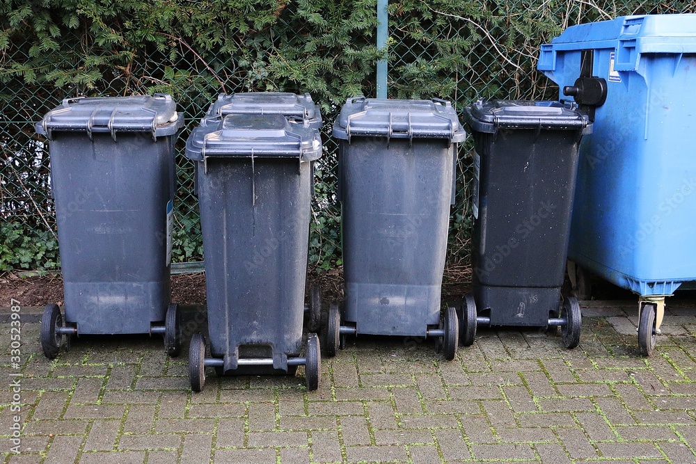 dark garbage cans are standing at the fence in a row dark garbage cans are standing at the fence in a row