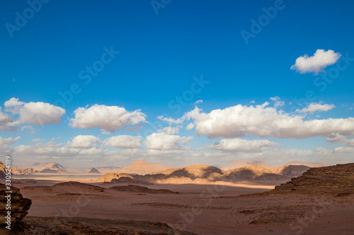 Fototapeta Naklejka Na Ścianę i Meble -  Kingdom of Jordan, Wadi Rum desert, sunny winter day scenery landscape with white puffy clouds and warm colors. Lovely travel photography. Beautiful desert could be explored on safari. Colorful image