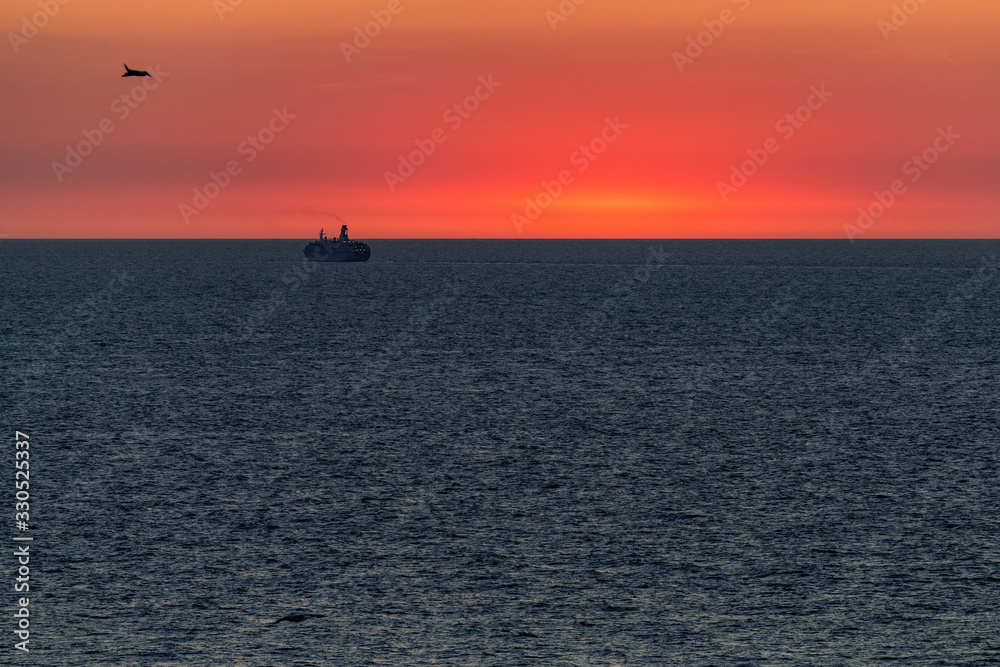 Silhouette of a large ocean liner sailing on the sea on the horizon after sunset.