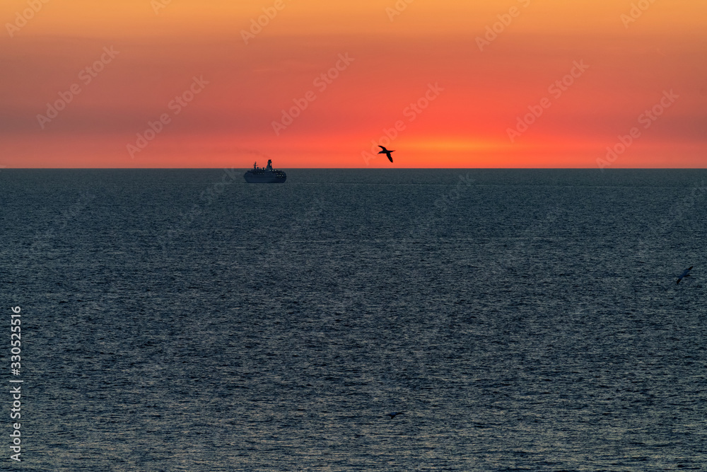 Silhouette of a large ocean liner sailing on the sea on the horizon after sunset.