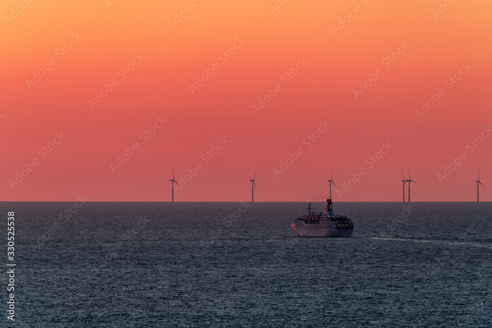 Large ocean liner sailing on the sea after sunset. On the horizon in the sea are wind power plants