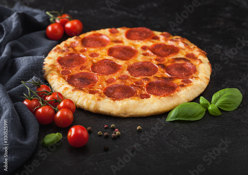 Fresh round baked Pepperoni italian pizza with tomatoes with basil on black background with grey linen towel.