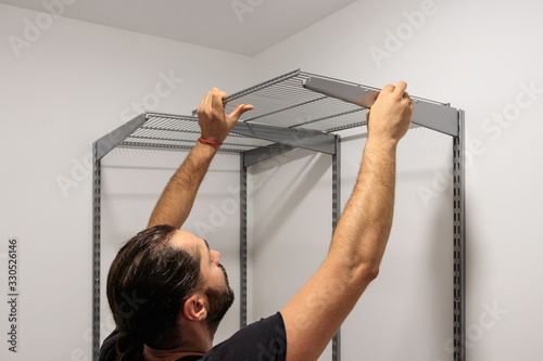 A working fitter man with a beard mounts metal racks on the wall.