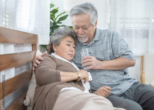Asian Senior Woman taking medicines and drinking water while sitting on couch. Old man take care his wife while her illness at the house.healthcare and medicine concept. © mkitina4