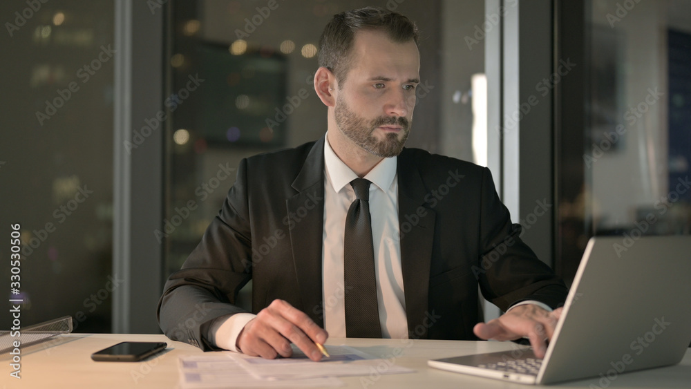 The Smart Businessman working on Laptop and Document at Night The Smart Businessman working on Laptop and Document at Night