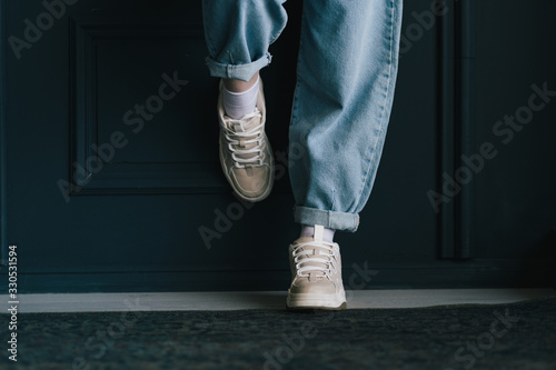 Closeup view photography of two female legs isolated at black wall background. Woman wearing trendy fashionable blue denim jeans and sneakers with lacing.