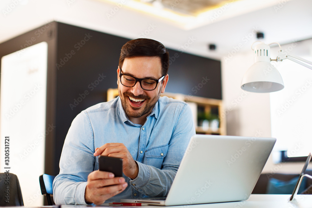 Young business man working at home with laptop and uses a smartphone - obrazy, fototapety, plakaty 