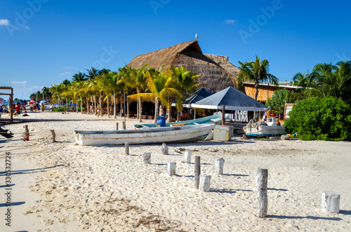 A Caribbean beach with a fishing boats tied up outside a coffee shop showing beep blue sky and a line of palm trees running along the shore side. . © Garry Basnett