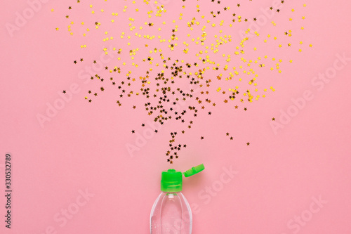 Fototapeta Naklejka Na Ścianę i Meble -  Transparent hand sanitizer with bursting confetti at pink background. Coronavirus prevention concept.