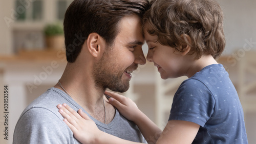 Close up of cute young father and little preschooler son look in eyes touch foreheads cuddle enjoy tender moment together, happy dad and sweet small boy child hug embrace show love and tenderness