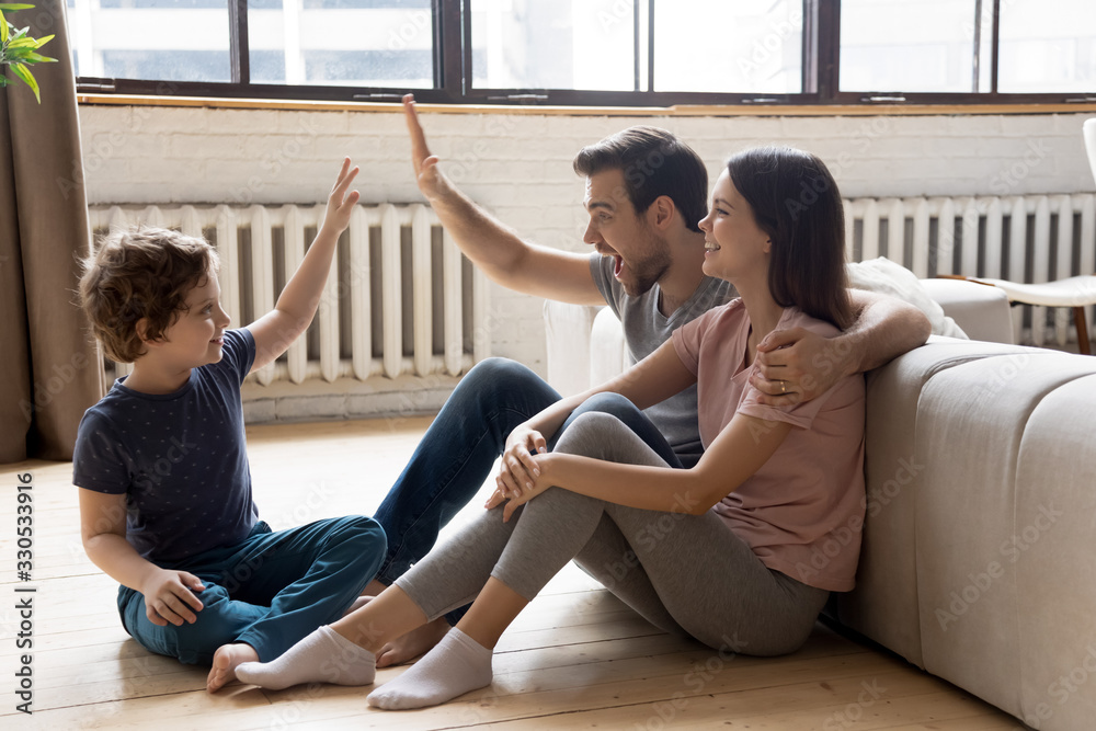 Happy young family with little child sit on warm wooden floor relaxing together in own apartment, overjoyed parents rest enjoy weekend have fun with small son excited to move to new home Happy young family with little child sit on warm wooden floor relaxing together in own apartment, overjoyed parents rest enjoy weekend have fun with small son excited to move to new home