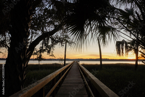 Sunset on Spring Island, South Carolina; view of a long dock leading out into the Callawassie River at sunset with palmetto trees and the marsh